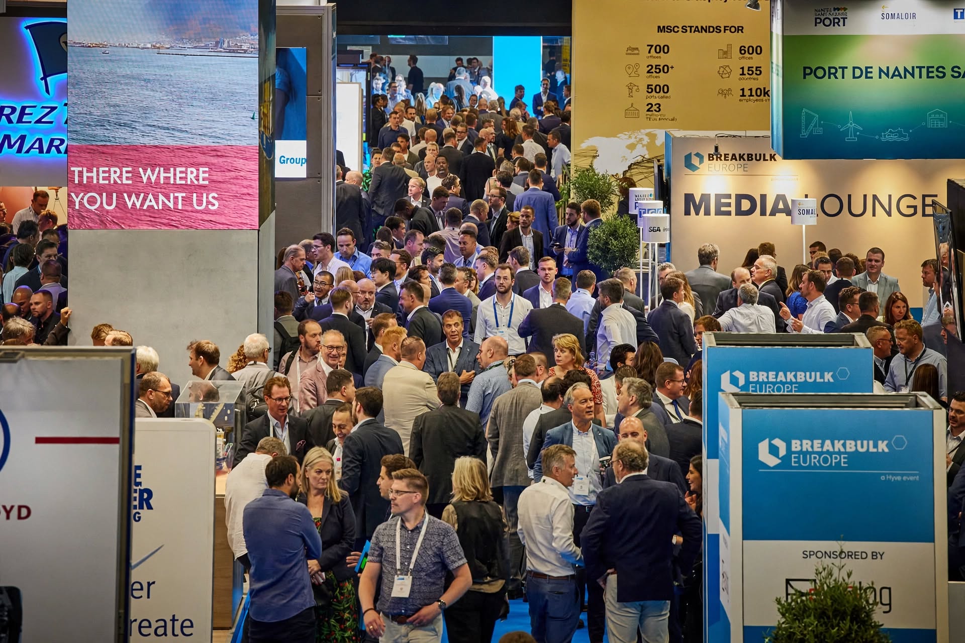 Volle beursvloer met bezoekers rond de mediazone van de beurs